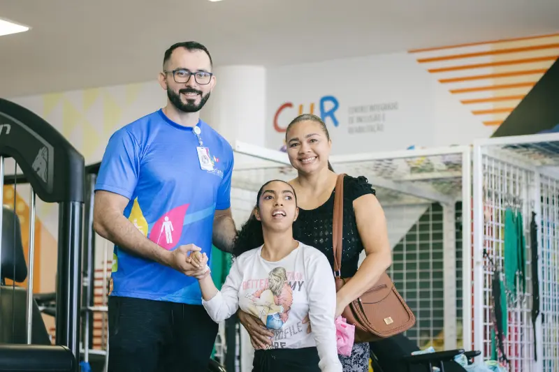 Débora Tavares acompanha a filha, Drisana Tavares, usuária com microcefalia assistida pela reabilitação ao lado do profissional de educação física, Samuel Pacheco.